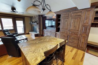 A spacious living area with a large stone fireplace, a flat screen TV, a table with chairs, and a couch.