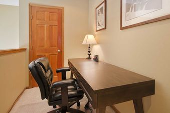 A home office featuring a dark wood desk, a comfortable black leather office chair, and a desk lamp, with two framed pictures on the light-colored walls.