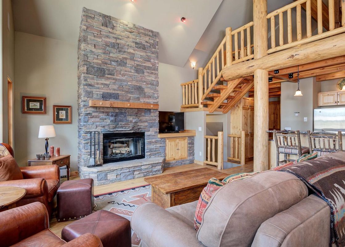 The spacious living room at Moonlight Basin Lodging 38A Cowboy Heaven features a stone fireplace and a large sectional couch in front of it.