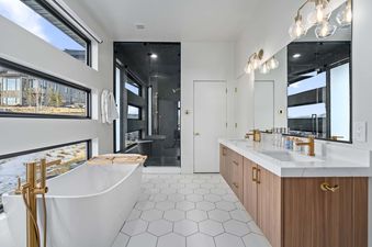 A modern bathroom with a white bathtub, a double vanity with a white countertop and brown cabinets, and a large shower with black tile.