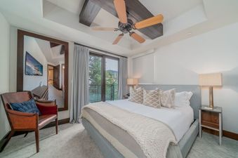 The Lumiere 2 Bedroom Suite bedroom features a comfortable king-size bed with white linens and plush pillows, a ceiling fan, and a view of the mountains.