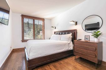 A bedroom with a white bed, wood floors, and a dresser with a plant on top