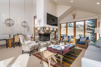 A living room with a fireplace, large windows, and a view of a mountain range.