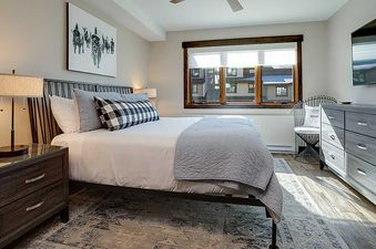 A modern bedroom in Ranch at Steamboat RA217 featuring a bed with white and gray bedding, two dark wood nightstands, a flat-screen TV, and a window.