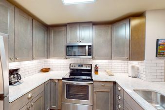 A modern kitchen in Trappeurs Lodge 1101 featuring grey cabinets, light countertops, and stainless steel appliances.