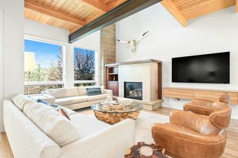 A bright and spacious living area with high ceilings, large windows, a modern fireplace, comfortable sofas, and leather armchairs.