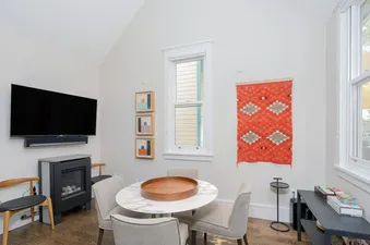 A modern dining and living area at The Hummingbird House with a white marble-top table, a flat-screen TV, and an electric fireplace.