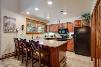 A fully equipped kitchen with wooden cabinets, black appliances, a central island with bar seating, and a large window providing natural light in Chateau Chamonix CX233.