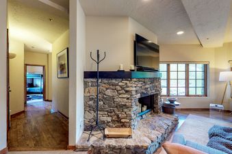 A living room with a stone fireplace in Westermere 310. There is a large flat-screen TV above the fireplace.