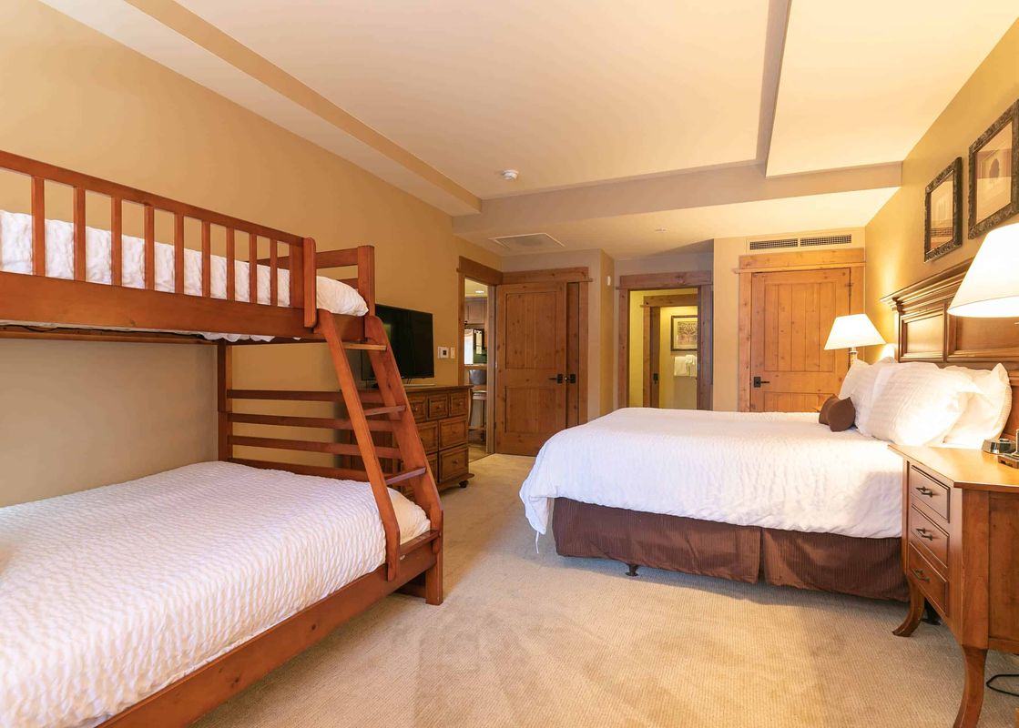 A bedroom with a bunk bed, a large bed, and a dresser with three drawers.