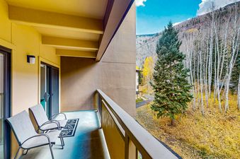 The balcony of Fallridge 302 features two chairs, a rug, and a view of the forest.