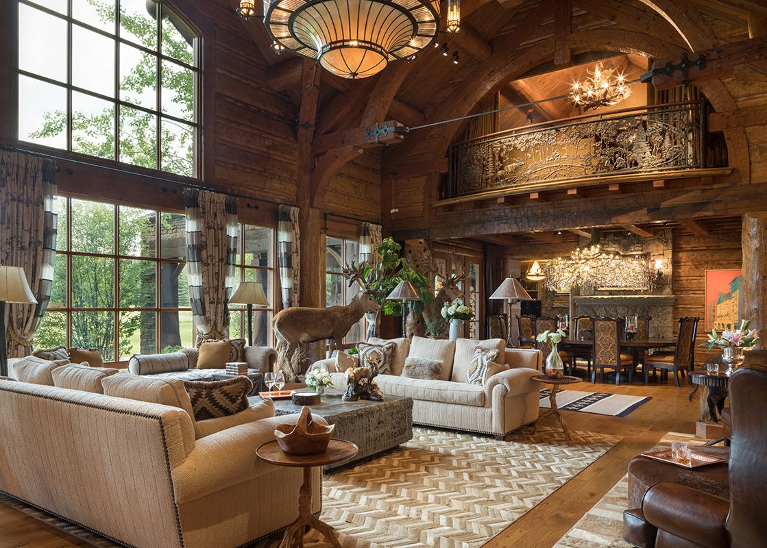 A spacious, rustic-chic living area in the Royal Wulff Lodge with large windows, wooden interiors, comfortable seating, and an elegant dining area, complete with decorative accents and an overlooking balcony.