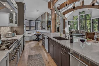 A spacious modern kitchen with a large island opening into a sunlit living room with vaulted timber ceilings at the Moose Meadows Reserve.