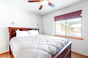 A bright bedroom features a large wooden bed with white bedding, two small bedside lamps, and a window offering a snowy outdoor view.