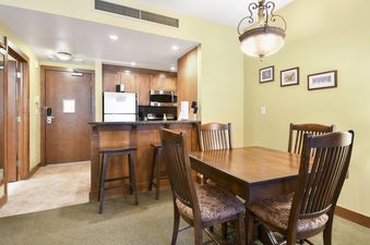 A cozy dining area with a wooden table and chairs, adjacent to a compact kitchen with wooden cabinets and stainless steel appliances, in the Sundial Lodge Studio.