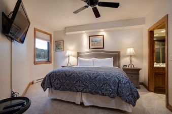 A king-sized bed with a blue and white patterned duvet is the centerpiece of this bedroom at Chateau Chamonix CX324, flanked by nightstands with lamps and a window offering an outdoor view.