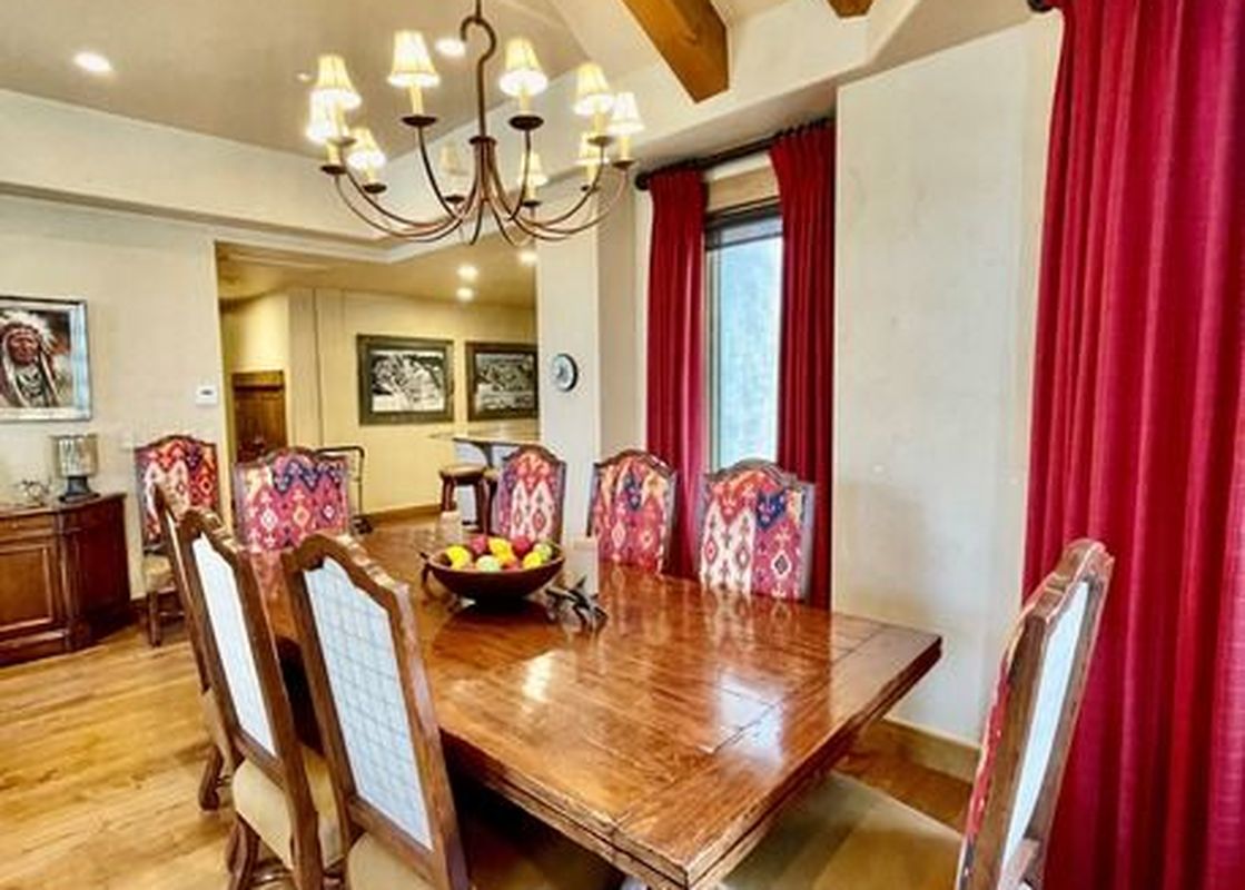 A large dining room with a long wooden table and eight chairs, illuminated by a large chandelier.