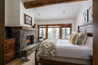 A cozy bedroom with a fireplace and a large bed, offering a view of a snowy landscape through expansive windows.