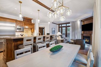 The kitchen and dining area of The Aspen 03B features an open layout with a large dining table, a beautiful wood island with bar stools, a fireplace, and access to a private patio.