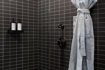 A modern shower at Mollie Aspen Cozy King with black subway tiles, a light blue bathrobe, and a wooden stool.