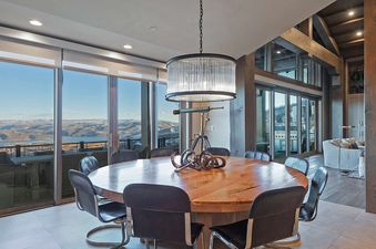 The dining area in Dreamscape 365 boasts a stylish, round wooden table illuminated by a modern chandelier.