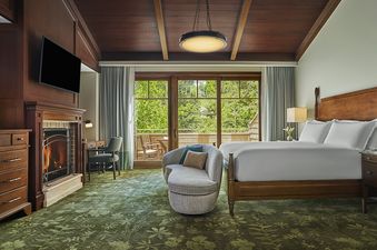 A cozy bedroom in the Montage Flagstaff Suite features a large bed, a fireplace, and a private balcony overlooking a lush green landscape.