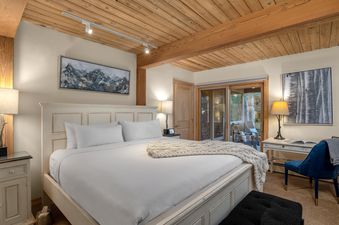 The cozy master bedroom of Trails 103 features a king-size bed, rustic wood ceiling, desk, and sliding doors to a patio.