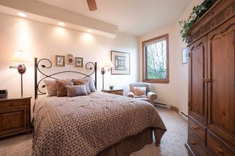 A cozy bedroom with a large bed, a wooden armoire, and a window offering an exterior view.