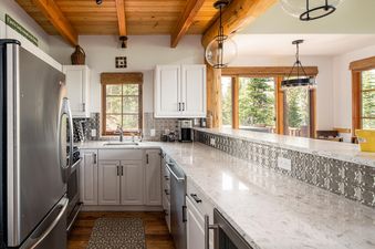 Moonlight Basin 7 Gambler kitchen features white cabinetry, stainless steel appliances, a farmhouse sink, and granite countertops.