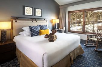 A cozy bedroom in the Teton Mountain Lodge and Spa Two Bedroom Bi-Level Suite, featuring a king bed and a rocking chair near a large window.