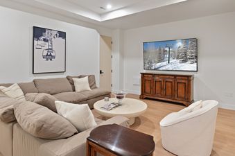A modern media room at SkyRidge 1843 with a brown sectional, flat-screen TV, and light wood flooring.
