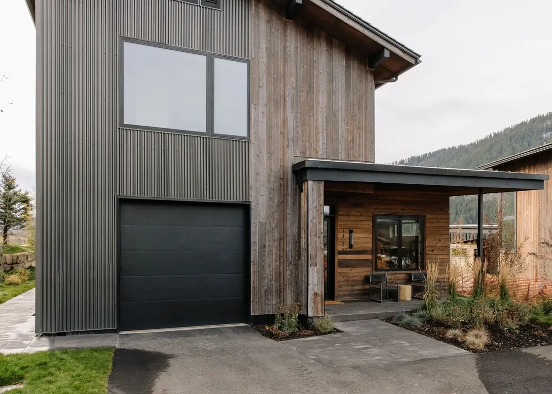 The Lodge Cabins features a modern rustic exterior with dark corrugated metal and warm wood siding, a large black garage door, and a welcoming covered entrance with outdoor seating.