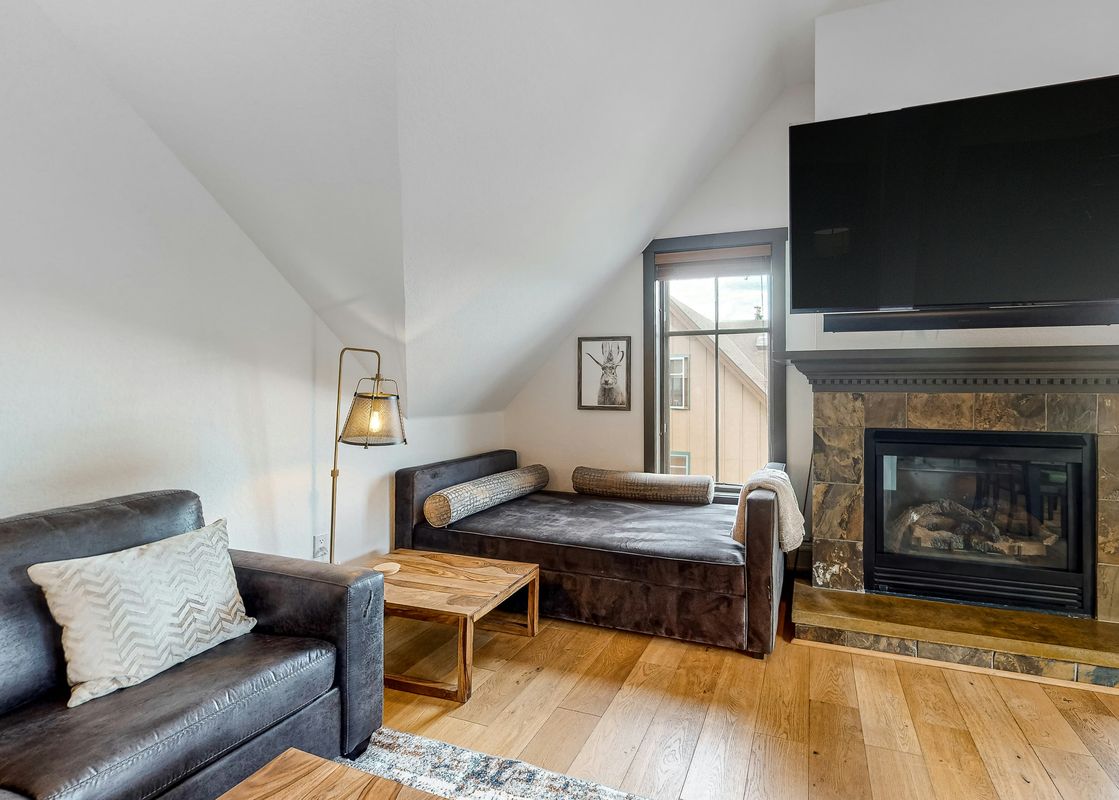 A cozy loft living area in Main Street Station 3405 with a leather sofa, chaise lounge, coffee table, fireplace, and flat-screen TV.