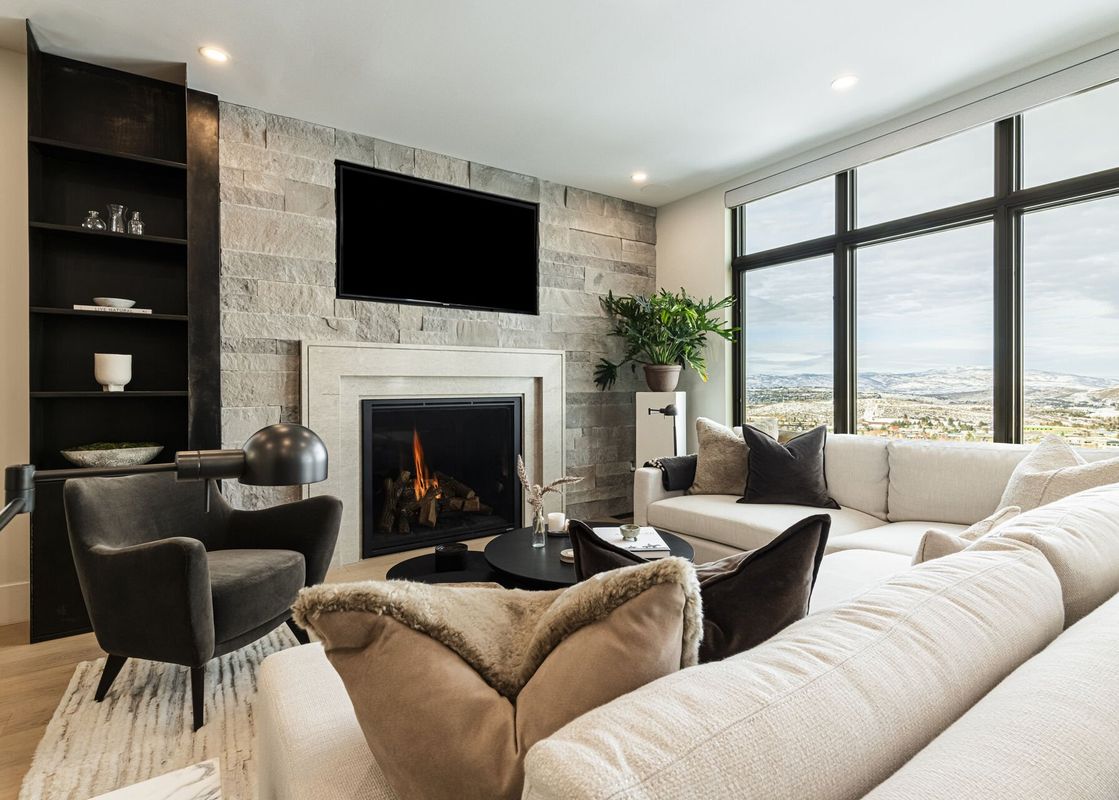 A luxurious living room at Frostwood Links with a fireplace, comfortable seating, and large windows overlooking snow-covered mountains.
