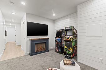 A game room with a fireplace, a flat-screen TV, two arcade games, and a chess board.