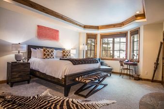A luxurious bedroom in Chateau Beaver Creek Residence 1304 featuring a king-sized bed, bay window with snowy views, and a zebra print rug.