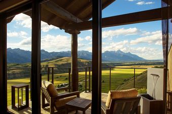 A luxurious private balcony of the Grand Teton Suite with wooden chairs and a table overlooks the Grand Teton mountains and a green valley under a blue sky.
