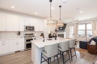 A modern white kitchen with a large quartz-topped island and barstools opening to a bright living area at Stage Coach.