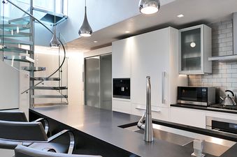 A modern kitchen with a stainless steel sink and a glass spiral staircase in the background.
