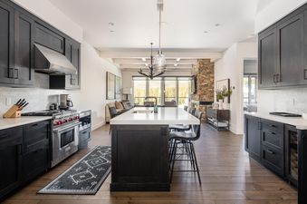 The modern kitchen at Moonlight Basin 16 Wildwood features stainless steel appliances, dark cabinetry, a center island with seating, and a large, bright window.