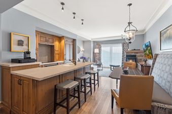 A spacious open-concept living area at St Regis 2 Bedroom Valley View, featuring a modern kitchen island with bar seating, a dining table, a cozy fireplace, and large windows with elegant drapes.