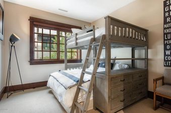 A cozy bunk bed room at Arrowleaf Lodge 109, featuring a sturdy wooden bunk bed with white and blue striped bedding, a large window, a modern black tripod lamp, and a decorative sign on the wall.