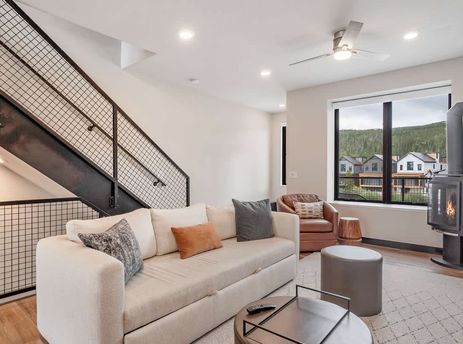 The contemporary living room features a comfortable sofa, a modern fireplace, and a large window overlooking a scenic mountain town.