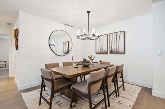 A modern dining table with six chairs in a white room with a mirror and artwork on the walls.