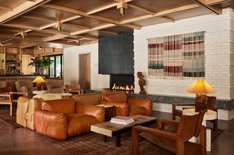 A cozy and elegant lounge area in the Mollie Aspen Shadow Mountain Suite featuring leather sofas, a lit fireplace, and a bar area.