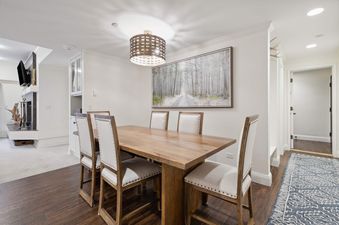 A dining area featuring a wooden table with six upholstered chairs, illuminated by a woven chandelier and recessed lighting.