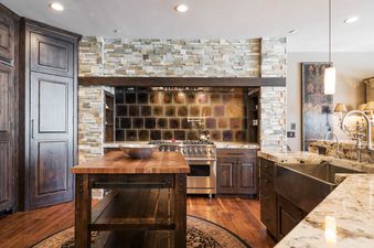 A luxurious gourmet kitchen at Harmony Haus, featuring dark wooden cabinets, granite countertops, a stone-clad range hood, and a large wooden island with a butcher block top.