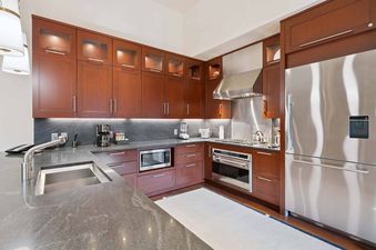 The contemporary kitchen features rich wooden cabinetry, stainless steel appliances, and sleek stone countertops, bathed in the soft glow of under-cabinet lighting.