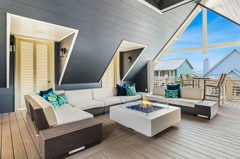 A stylish covered outdoor lounge area with an L-shaped sofa, a fire pit table, and views of residential homes.