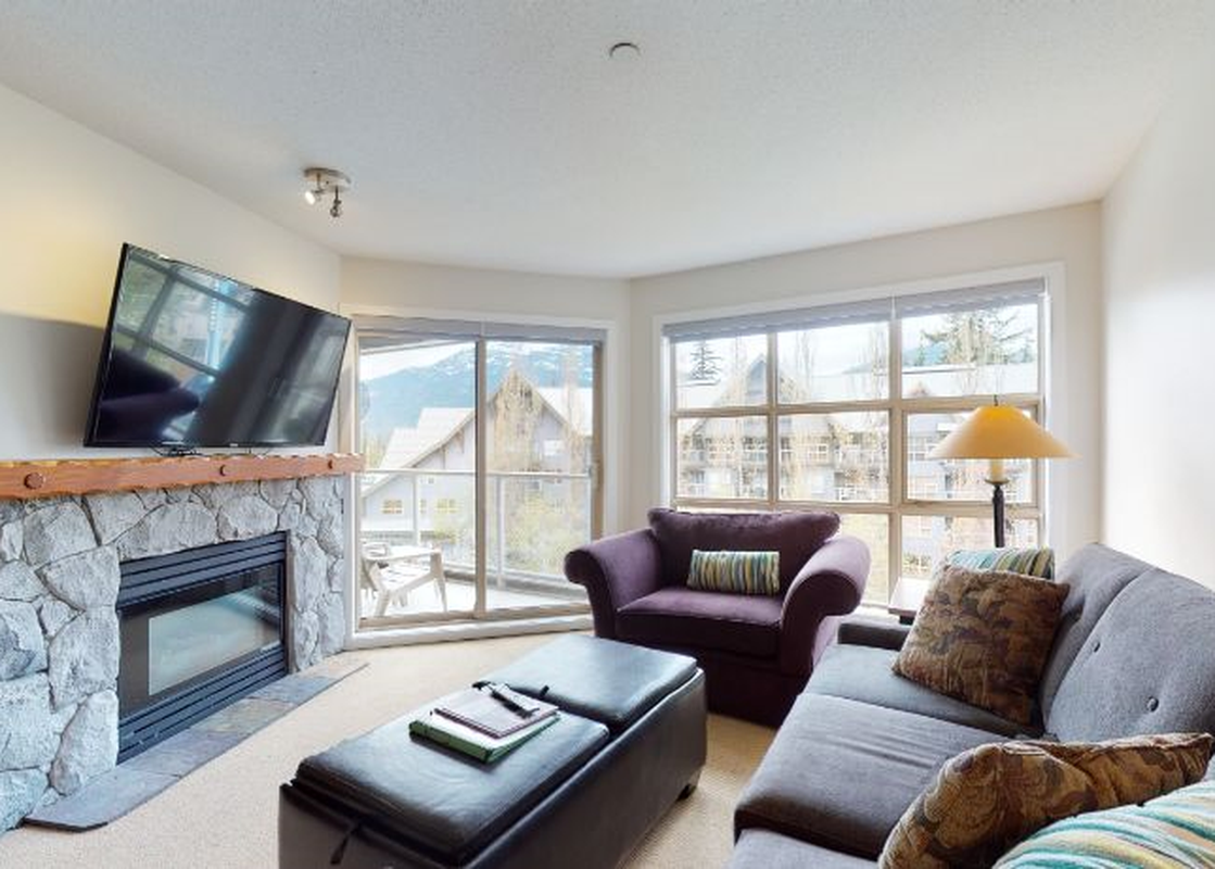 A cozy living room at Aspens on Blackcomb Unit 461 with a stone fireplace, large television, and comfortable seating.
